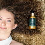 A person with brown curly hair laying down on a light coloured curly rug, with their hair on the rug and the Olew Hold Spray laid on top of their curls.
