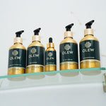 The Olew hair care range together on a glass shelf. The items shown are the Curl Defining Gel, Shampoo, Original Oil, Curl Cream and Conditioner.