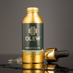 The Gold and black pipette top is laid behind the Olew Original Hair Oil bottle, on a dark grey background