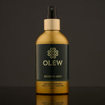 Olew Refresh Hair Mist, refreshing vegan haircare which is SLS and Paraben Free in a gold and dark green bottle, and a spray pump on top. The image has been taken on a grey background