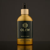 Olew Refresh Hair Mist, refreshing vegan haircare which is SLS and Paraben Free in a gold and dark green bottle, and a spray pump on top. The image has been taken on a grey background