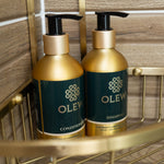 The Olew Conditioner and Shampoo in the gold and dark green bottles sat inside a gold shower caddy