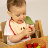 A baby eating strawberries and wearing the Oli & Carol Peppa the apple organic cotton baby bib available at Babipur 