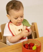 A baby eating strawberries and wearing the Oli & Carol Peppa the apple organic cotton baby bib available at Babipur 