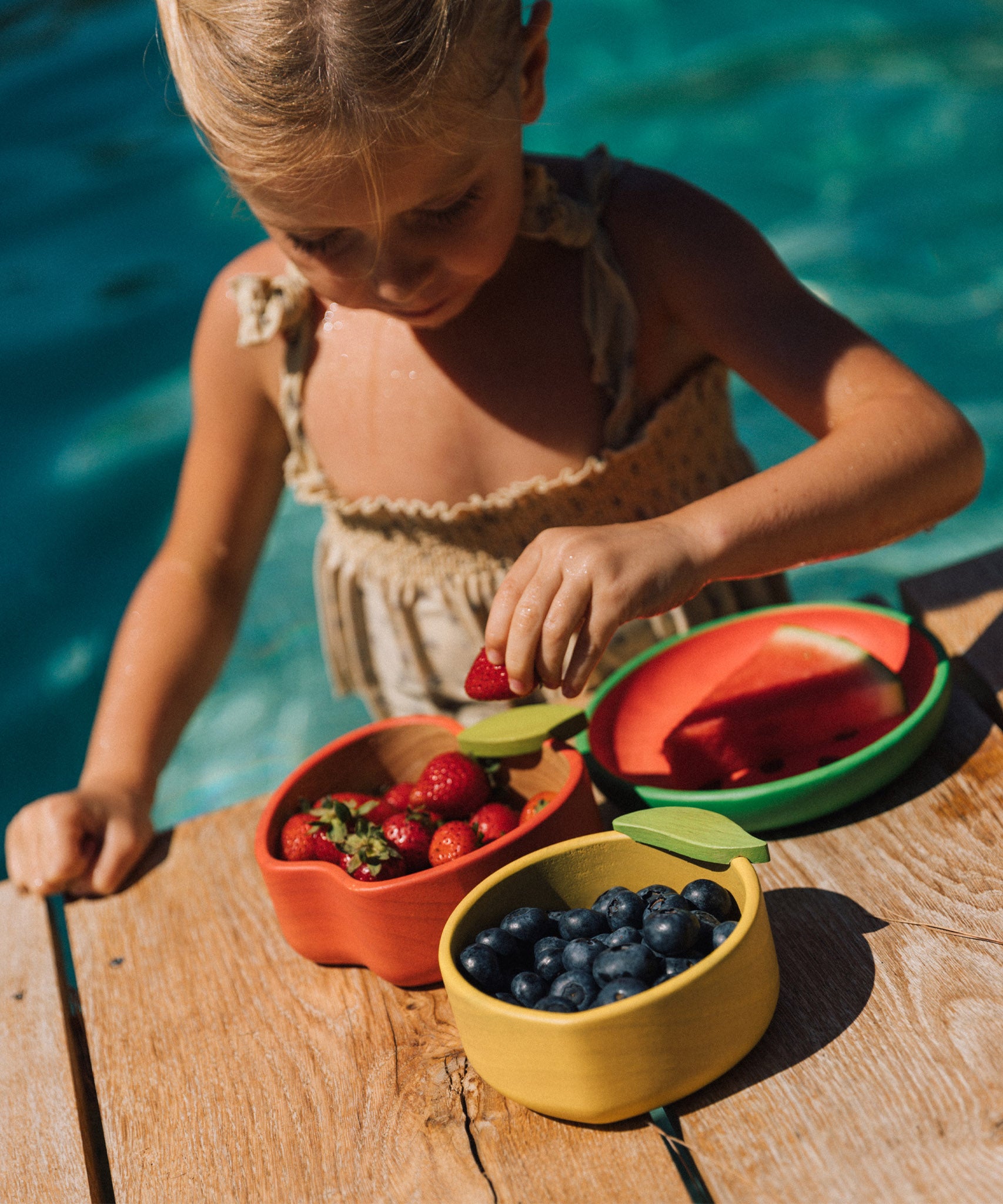 A child eating strawberries from the Oli & Carol Peppa the apple wooden bowl next to a lemon bowl available at Babipur. 