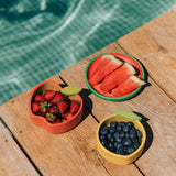 The Oli & Carol Peppa the apple wooden bowl next to a lemon bowl and watermelon plate filled with fruit. available at Babipur. 
