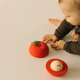 A baby playing with the Oli & Carol red apple stacking toy rattle ball available at Babipur. Showing the two halves and the removable core inside