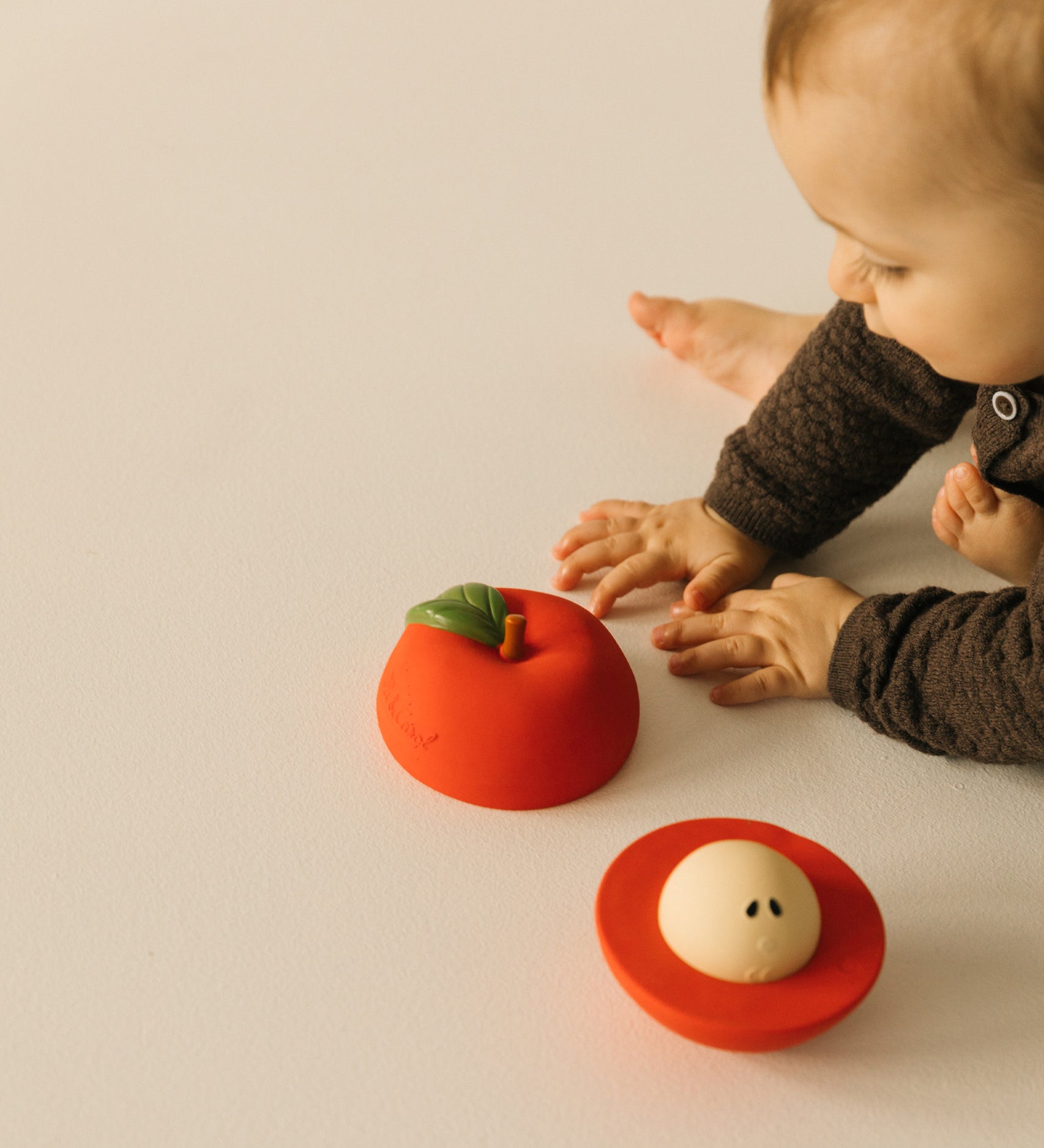 A baby playing with the Oli & Carol red apple stacking toy rattle ball available at Babipur. Showing the two halves and the removable core inside