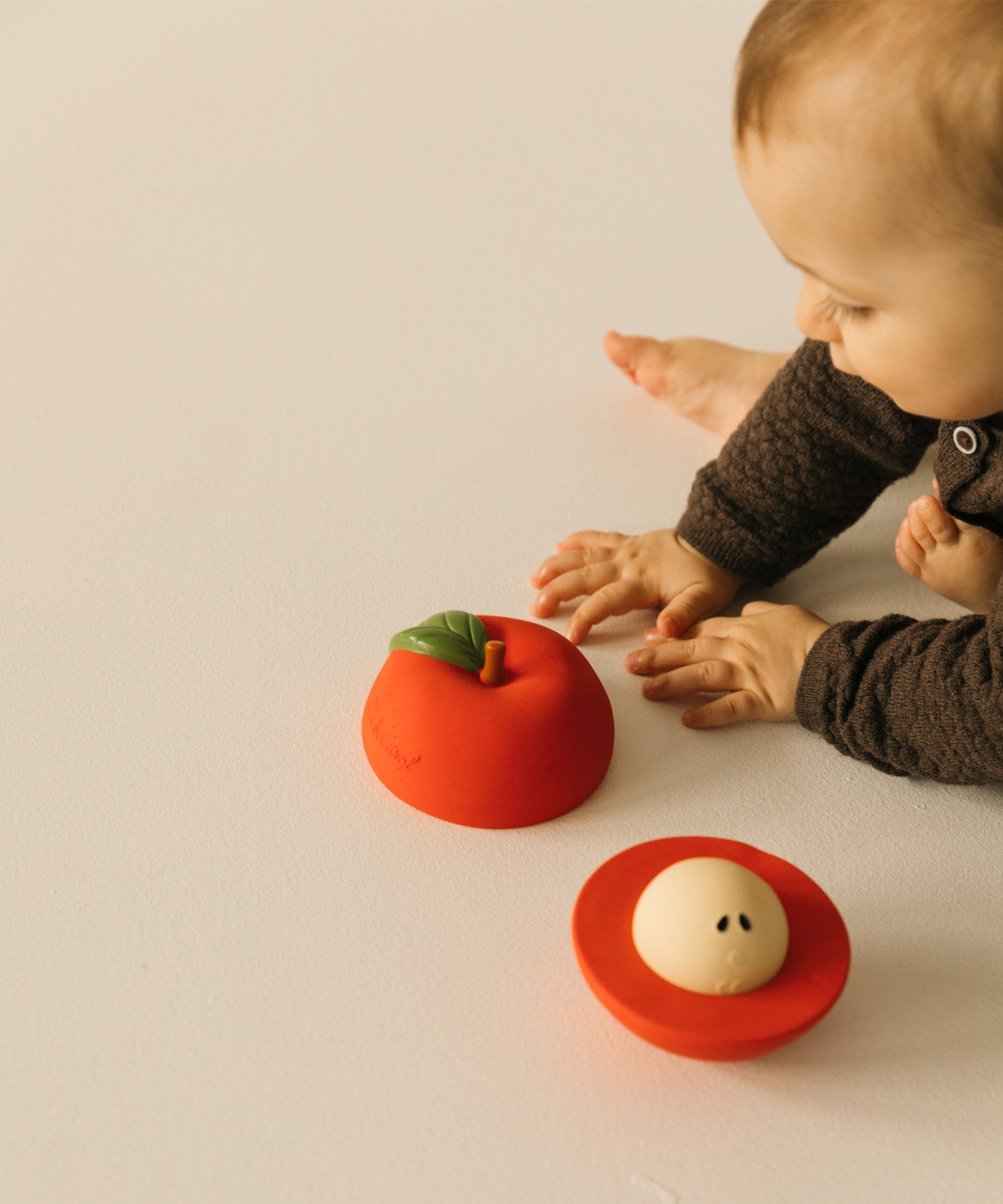 A baby playing with the Oli & Carol red apple stacking toy rattle ball available at Babipur. Showing the two halves and the removable core inside