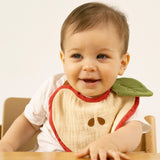 A baby sitting in a high chair and wearing the Oli & Carol Peppa the apple organic cotton baby bib available at Babipur 