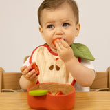 A baby sitting on a wooden high chair and  eating strawberries from the Oli & Carol Peppa the apple wooden bowl  available at Babipur. 
