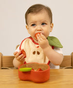 A baby sitting on a wooden high chair and  eating strawberries from the Oli & Carol Peppa the apple wooden bowl  available at Babipur. 