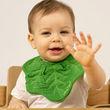 A baby sitting in a high chair and wearing the Oli & Carol Kendall the kale organic cotton baby bib available at Babipur 