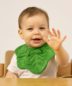 A baby sitting in a high chair and wearing the Oli & Carol Kendall the kale organic cotton baby bib available at Babipur 