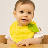 A baby sitting in a wooden high chair  and wearing the Oli & Carol Lou the lemon baby bib available at Babipur. 