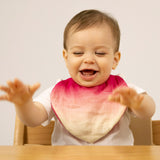 A baby sitting in a high chair and wearing the Oli & Carol Ramona the radish organic cotton baby bib available at Babipur 
