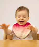 A baby sitting in a high chair and wearing the Oli & Carol Ramona the radish organic cotton baby bib available at Babipur 