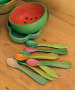 OIi & Carol wooden baby weaning spoons on a wooden surface next to a watermelon bowl. Both 2 packs are available at Babipur.