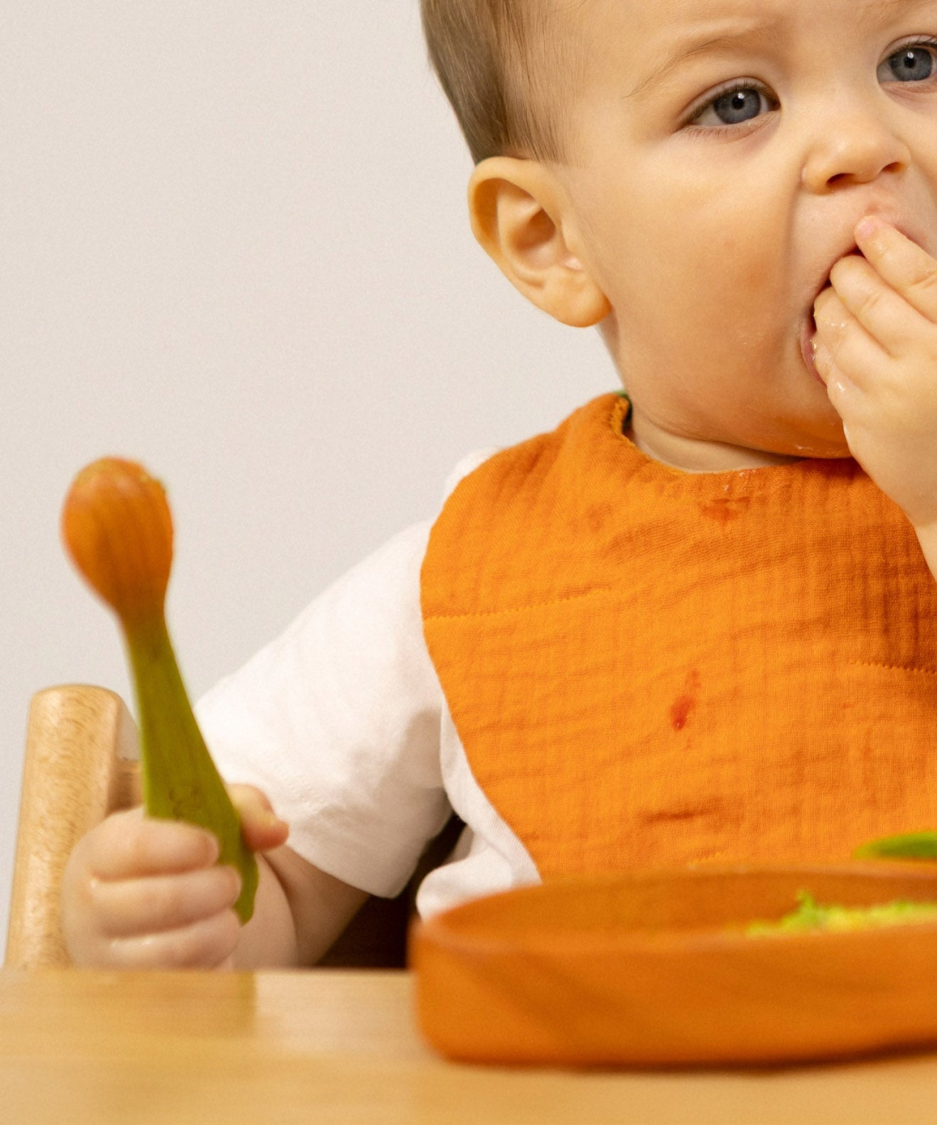 A baby holding the carrot design Oli & Carol wooden baby spoon available at Babipur.
