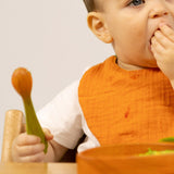 A baby holding the carrot design Oli & Carol wooden baby spoon available at Babipur.