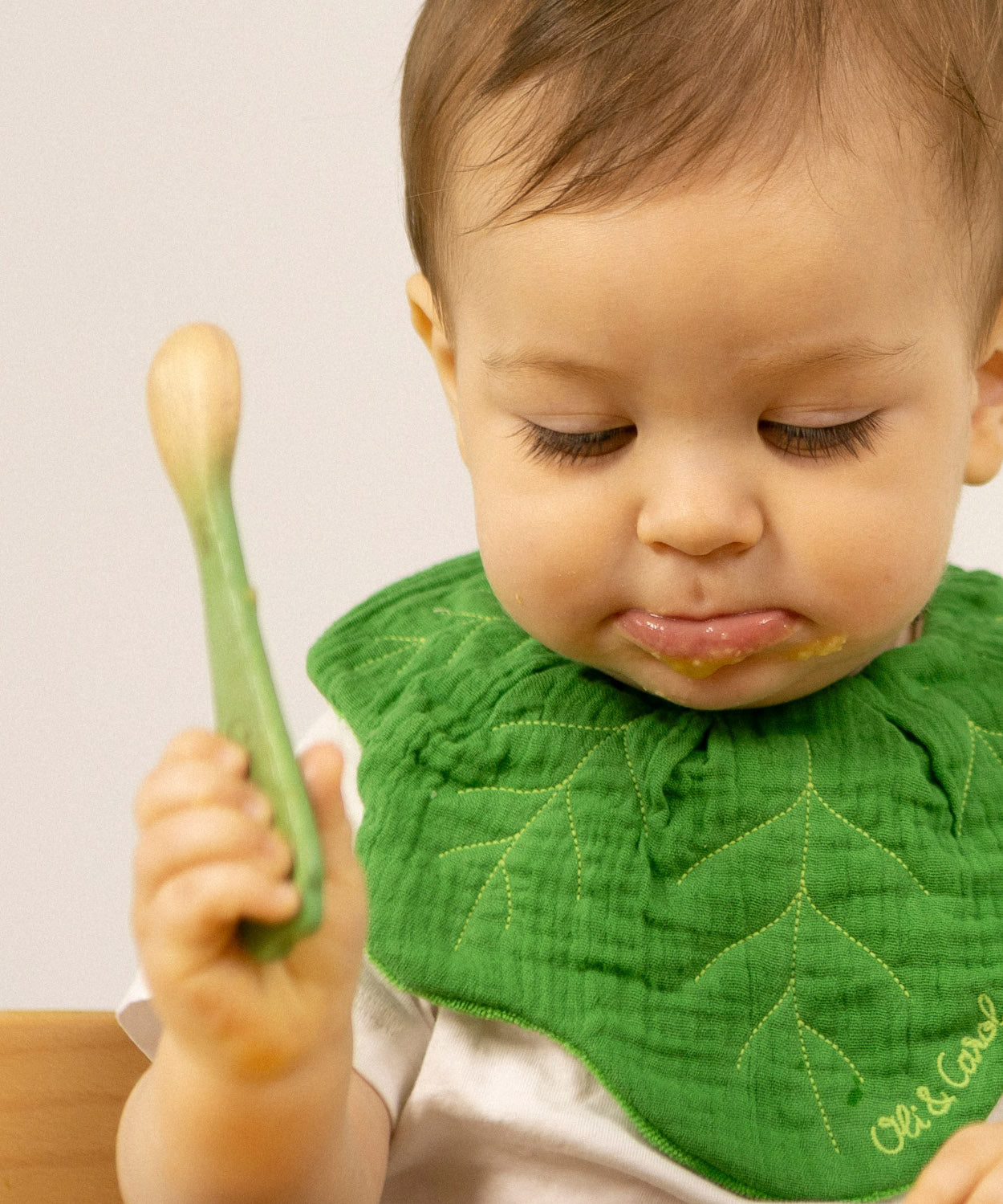 A baby holding the leek design Oli & Carol wooden baby spoon available at Babipur.