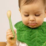 A baby holding the leek design Oli & Carol wooden baby spoon available at Babipur.