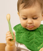 A baby holding the leek design Oli & Carol wooden baby spoon available at Babipur.