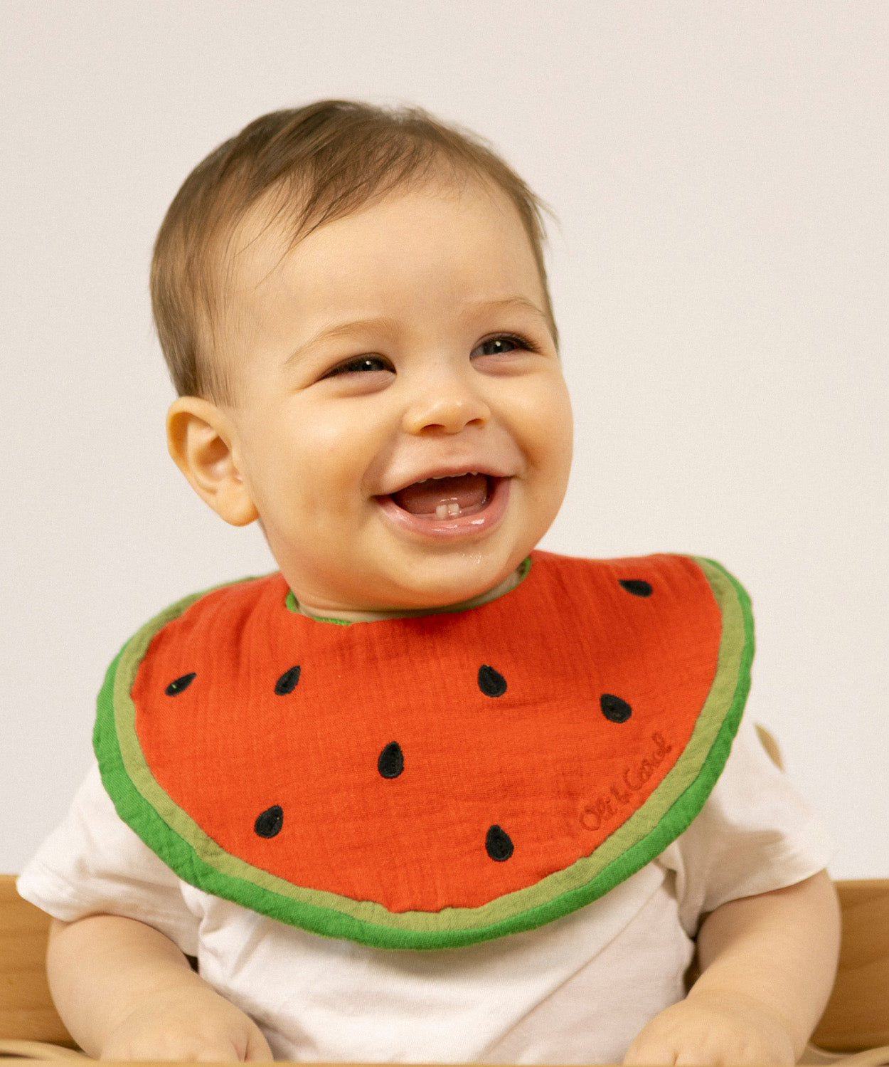 A baby wearing the Oli & Carol Wally the watermelon organic cotton baby bib available at Babipur 