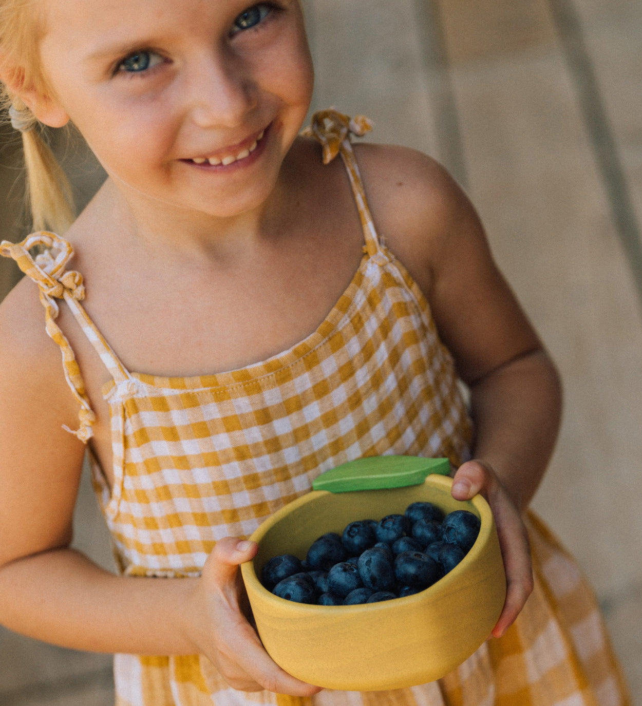 A child holding the Oli & Carol Lou the lemon wooden bowl filled with blueberries. Bowl available at Babipur. 
