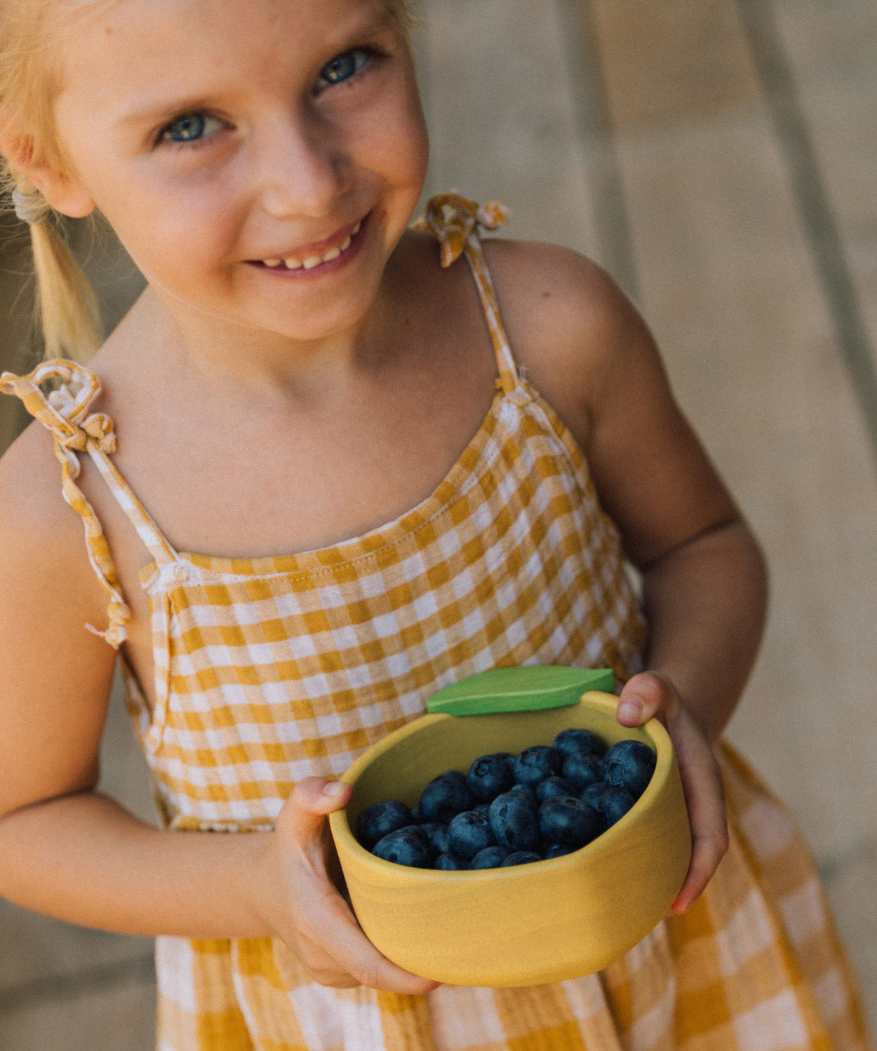 A child holding the Oli & Carol Lou the lemon wooden bowl filled with blueberries. Bowl available at Babipur. 