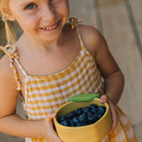 A child holding the Oli & Carol Lou the lemon wooden bowl filled with blueberries. Bowl available at Babipur. 