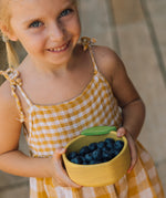 A child holding the Oli & Carol Lou the lemon wooden bowl filled with blueberries. Bowl available at Babipur. 