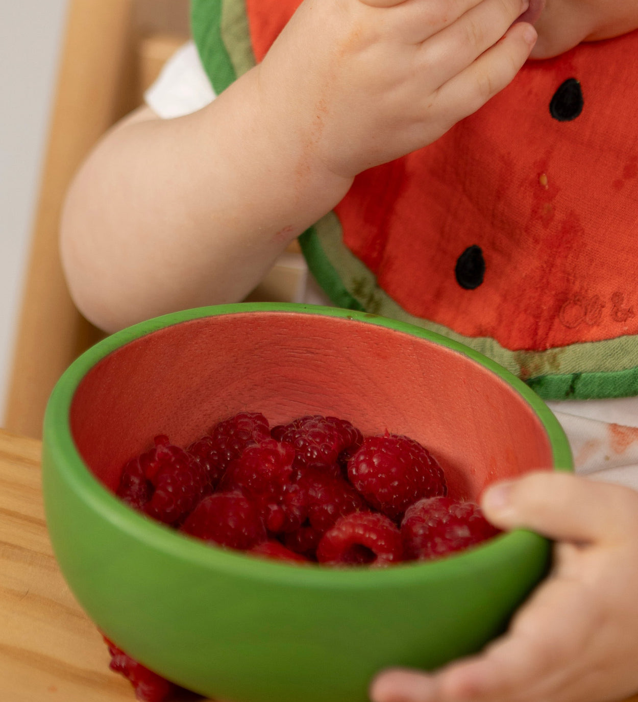 A close of a baby eating raspberries from the Oli & Carol Wally the watermelon wooden bowl  available at Babipur.  
