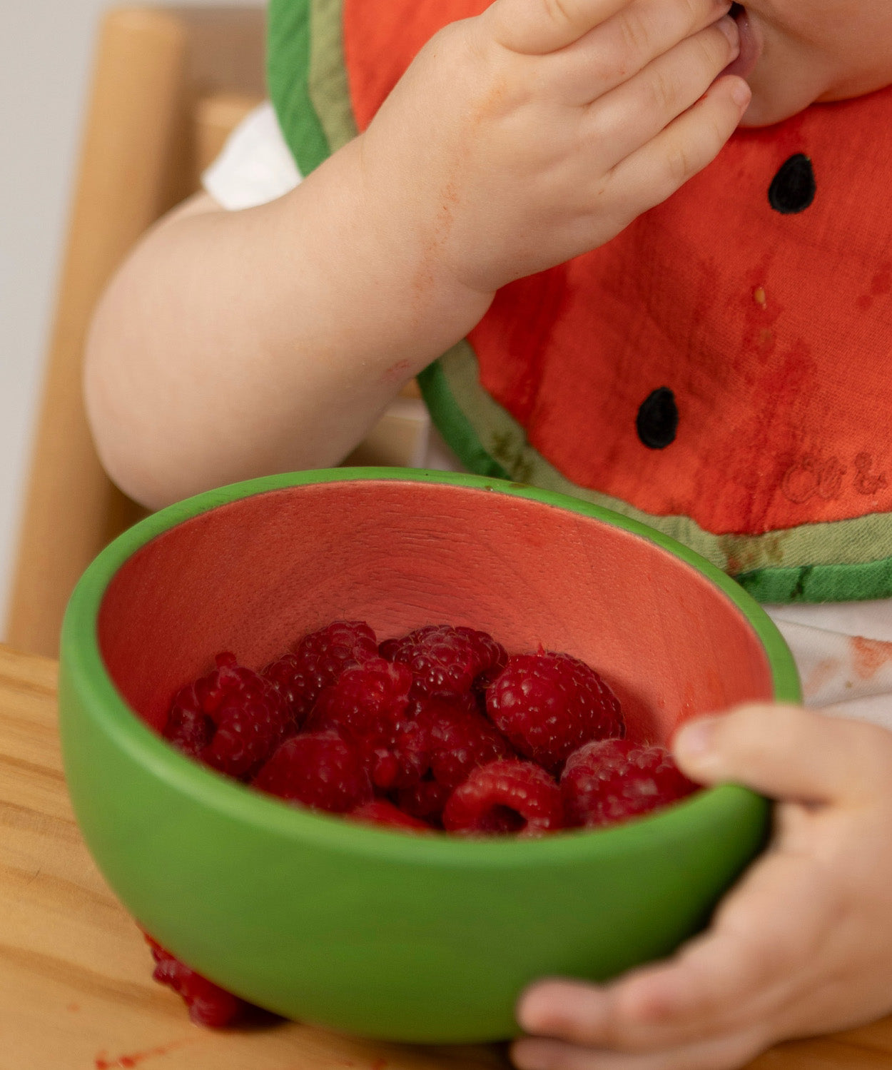 A close of a baby eating raspberries from the Oli & Carol Wally the watermelon wooden bowl  available at Babipur.  