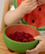 A close of a baby eating raspberries from the Oli & Carol Wally the watermelon wooden bowl  available at Babipur.  