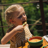 A child eating soup from the Oli & Carol Wally the watermelon wooden bowl and spoon set available at Babipur. 