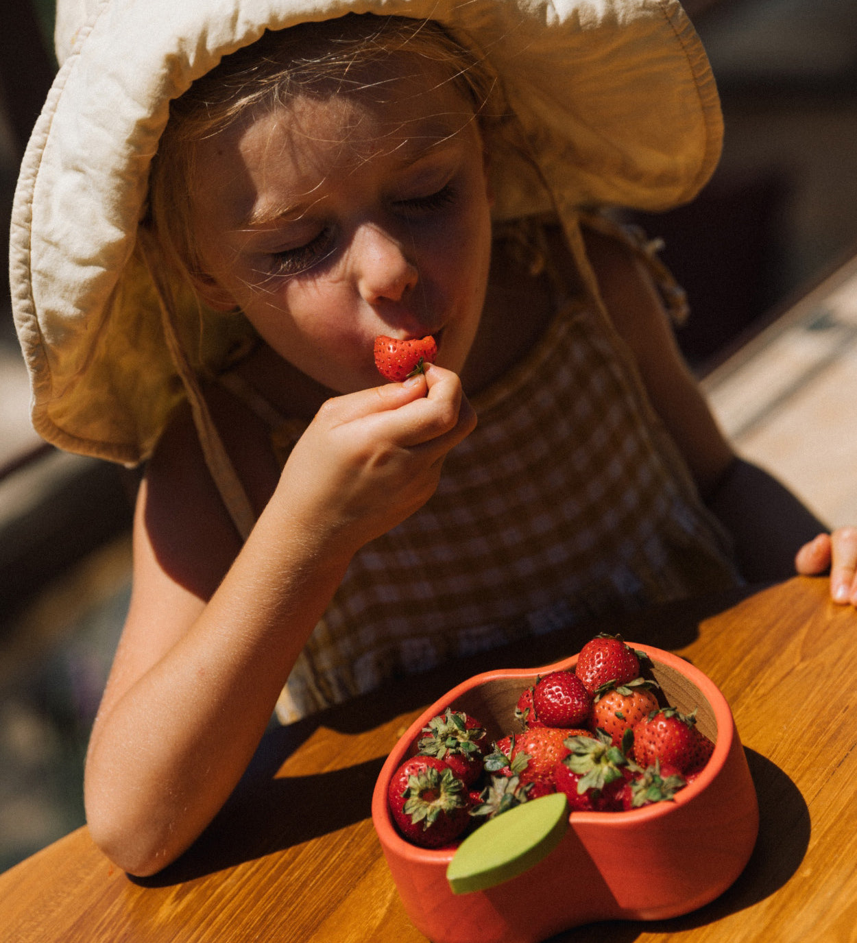 A child eating strawberries from the Oli & Carol Peppa the apple wooden bowl  available at Babipur. 