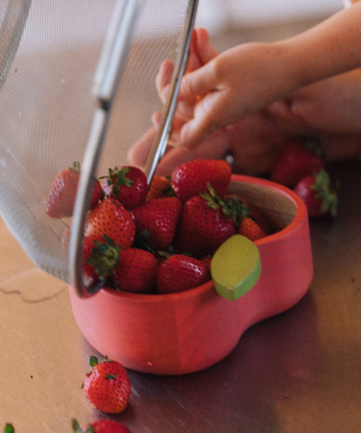 A close up of strawberries being tipped in the Oli & Carol Peppa the apple wooden bowl. Bowl available at Babipur. 