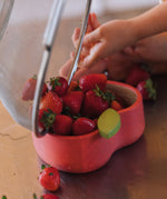 A close up of strawberries being tipped in the Oli & Carol Peppa the apple wooden bowl. Bowl available at Babipur. 