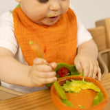 A baby eating and wearing the Oli & Carol Cathy the carrot organic cotton baby bib available at Babipur 