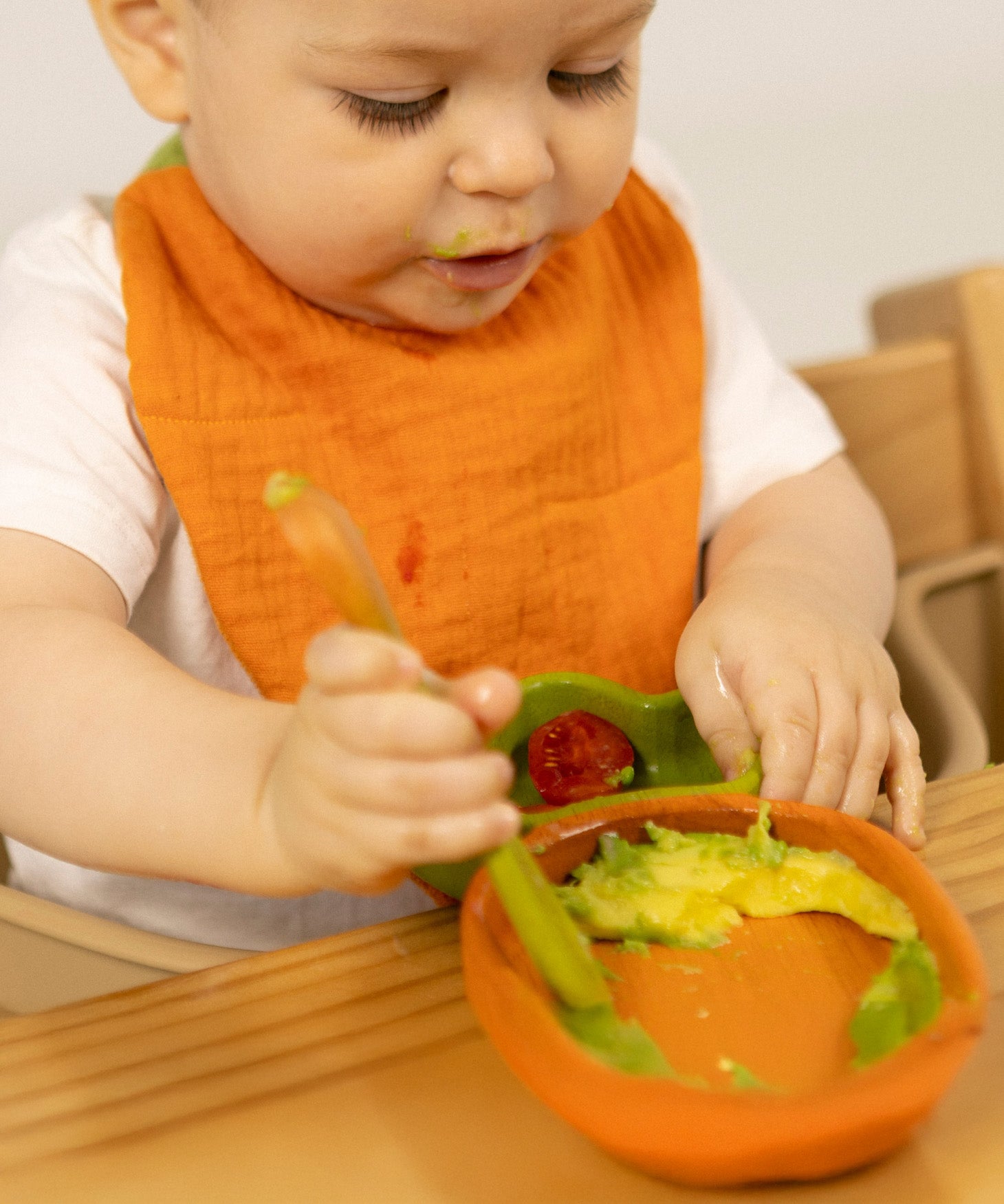 A baby eating and wearing the Oli & Carol Cathy the carrot organic cotton baby bib available at Babipur 