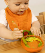 A baby eating and wearing the Oli & Carol Cathy the carrot organic cotton baby bib available at Babipur 