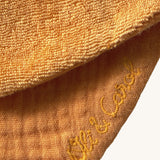 A close up of the  Oli & Carol Peppa the Cathy the carrot baby bib available at Babipur showing the brand name stitch detail on the inside of the bib