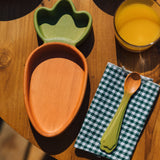 A close up of the Oli & Carol Cathy the carrot wooden plate and spoon on a table available at Babipur. 