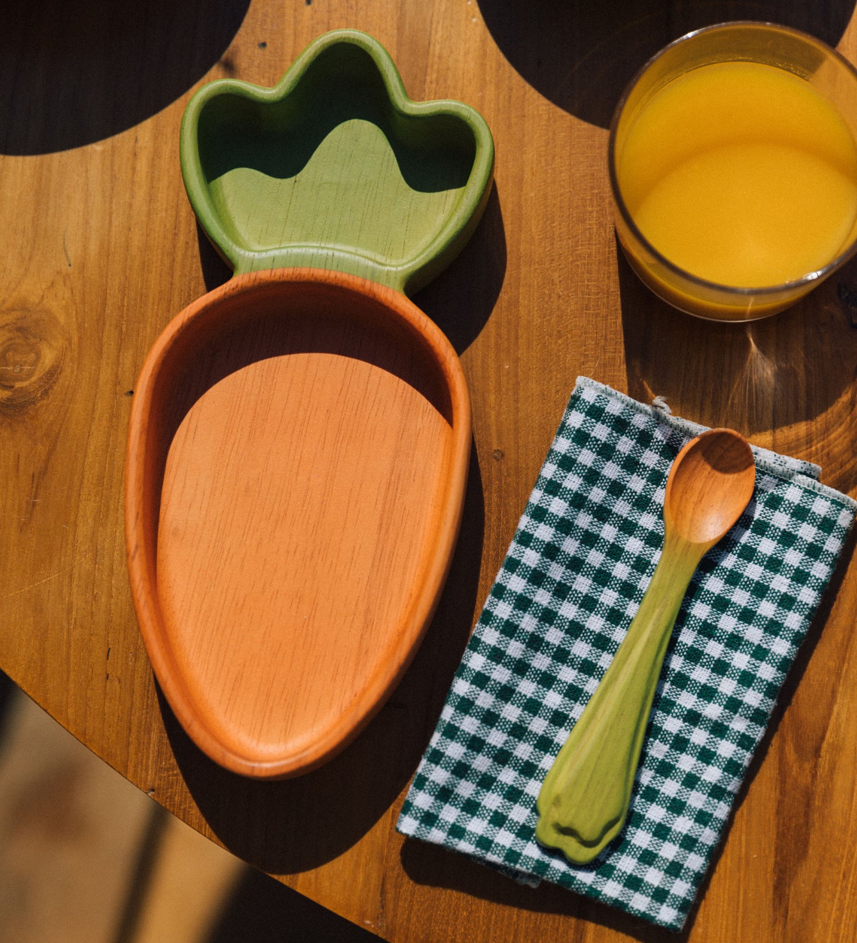 A close up of the Oli & Carol Cathy the carrot wooden plate and spoon on a table available at Babipur. 