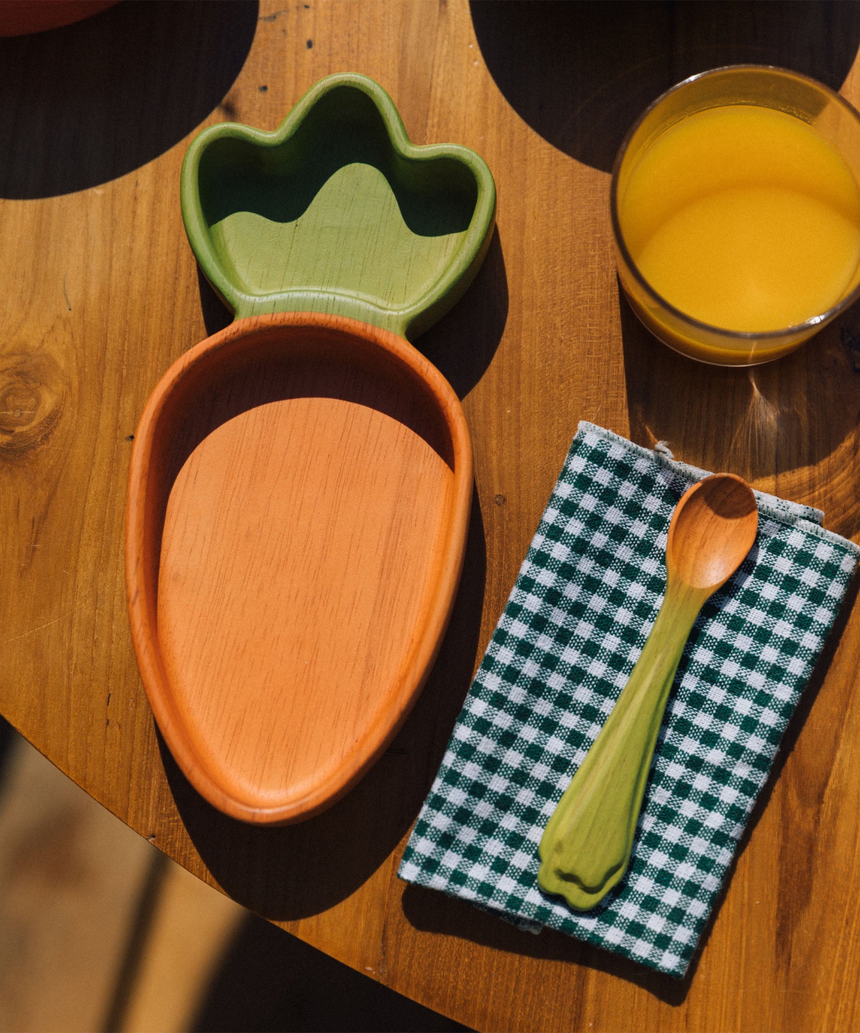 A close up of the Oli & Carol Cathy the carrot wooden plate and spoon on a table available at Babipur. 