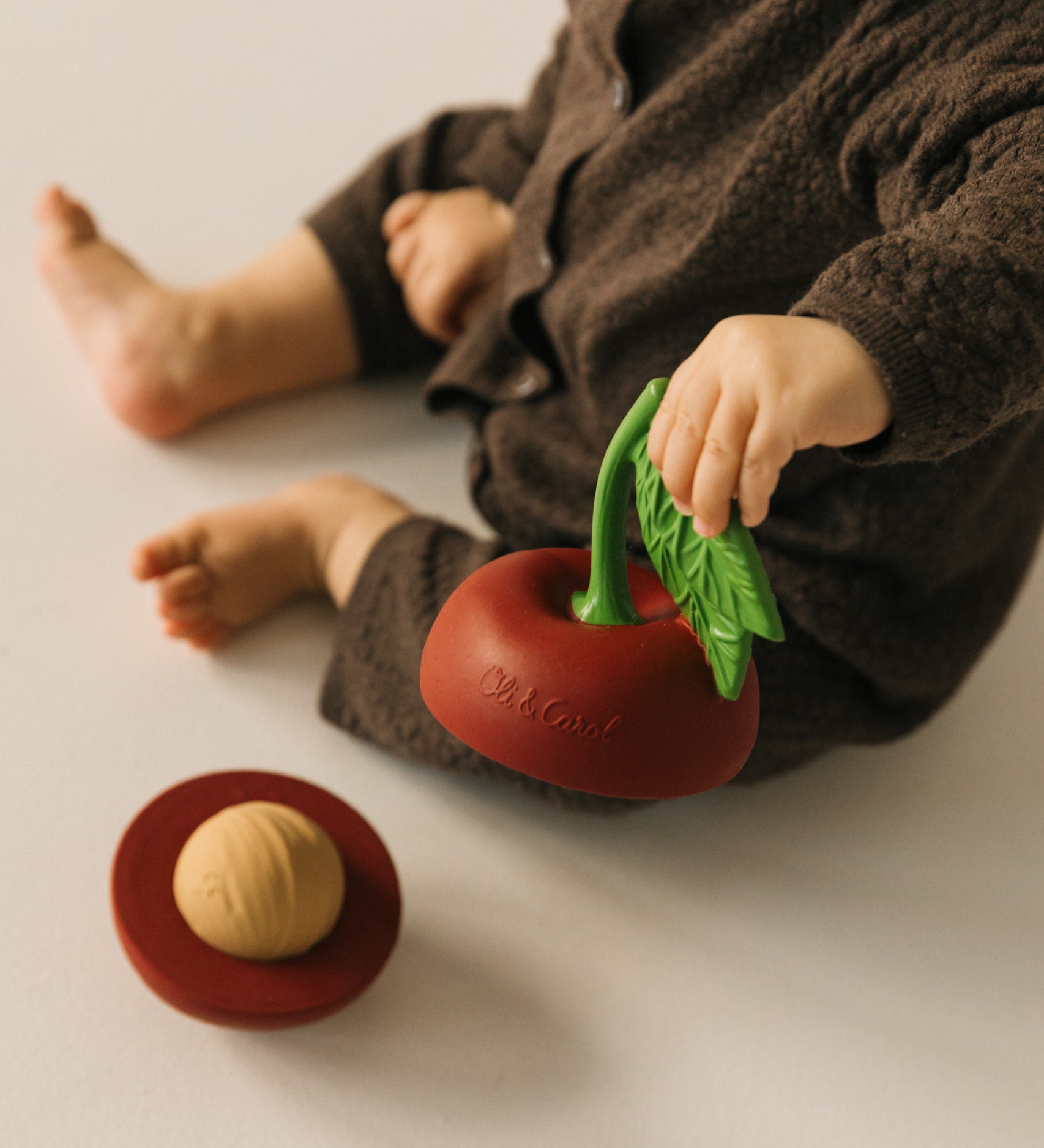 A baby holding one half of the Oli & Carol cherry stacking toy rattle ball available at Babipur.