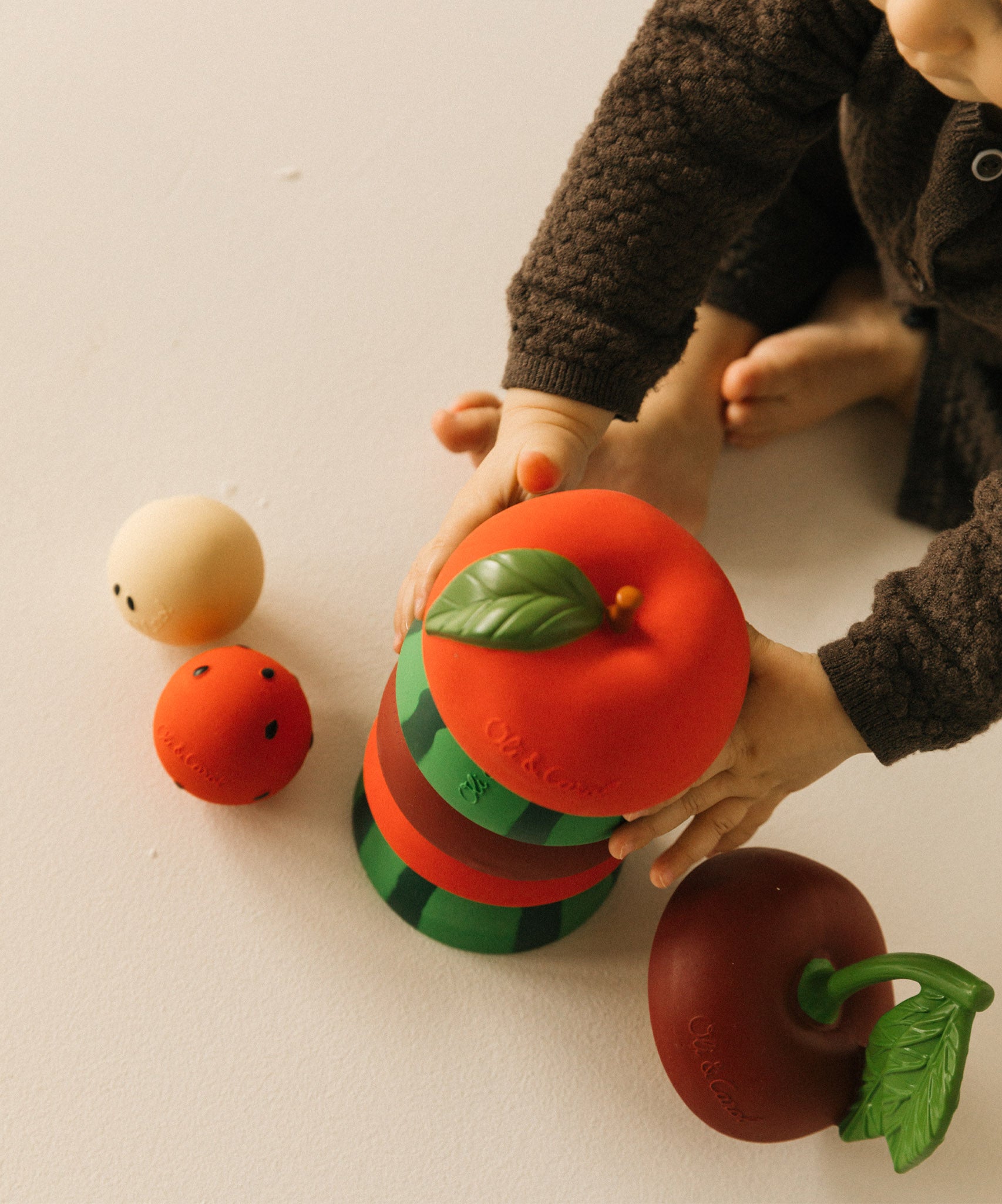 A child stacking the apple, watermelon and cherry Oli & Carol stacking toy rattles. Each fruit is available at Babipur.