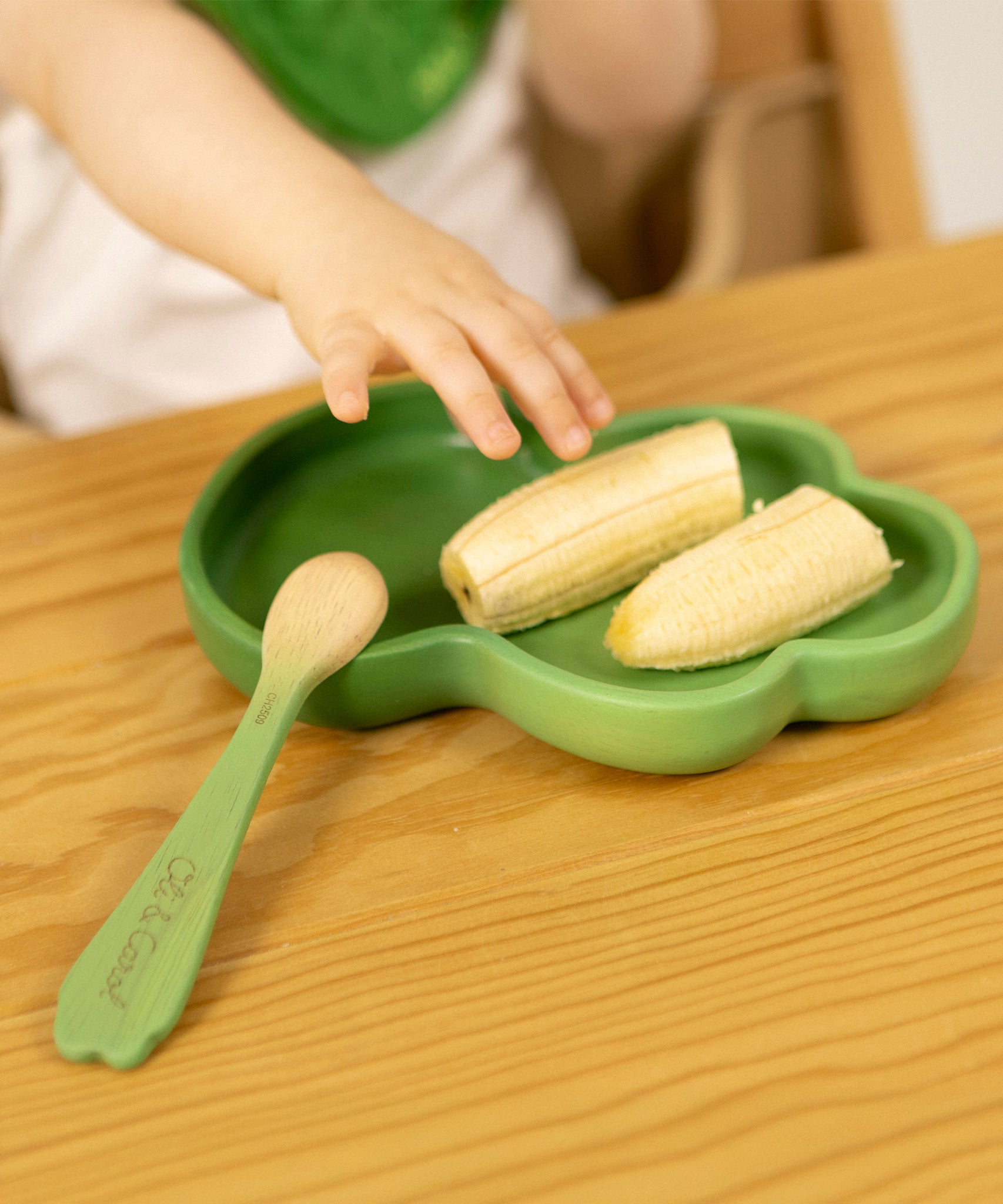 Childs hand reaching out for a banana on a rubber wood Kendall Kale plate for kids by Oli and Carol, for sale at Babipur.
