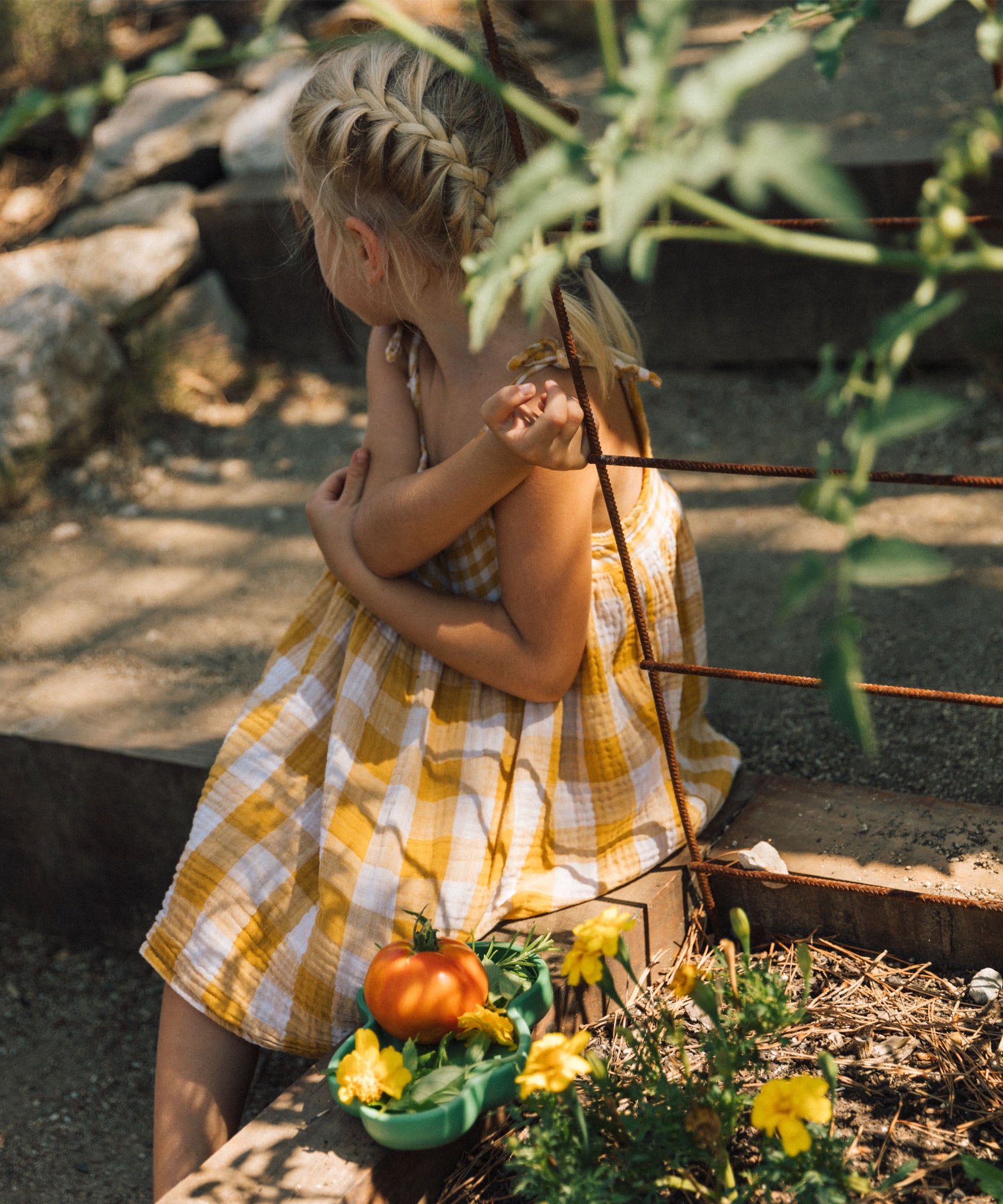 A child sitting on a stone surface next to the Oli & Carol wooden kale plate filled with vegetables available at Babipur.